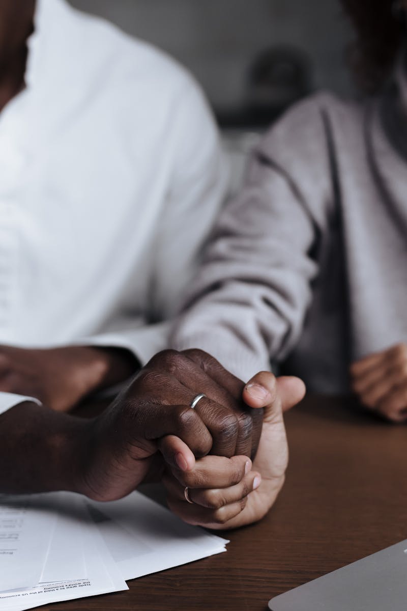 A diverse couple holding hands over documents on a table indoors.